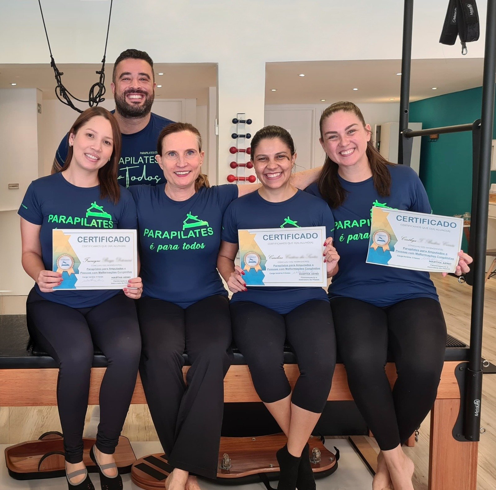 Participantes do workshop de fevereiro de 2024 sorrindo e segurando seus certificados, sentados em um aparelho de Pilates.